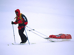imagen emblemática de una travesía polar, el explorador, su trineo, el sistema de arnés y los skis en un blanco inmenso.